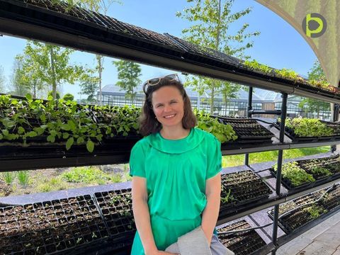 Dr Maryna Kuzmenko, founder of Petiole, smiling in front of shelves of seedling trays outside a greenhouse.
